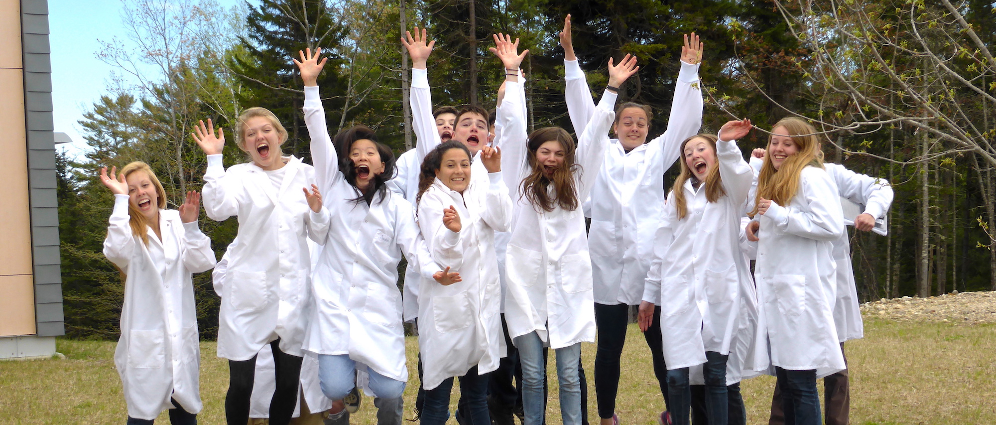 Students outside with lab coats on and hands in the air.